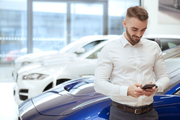 Homem bonito, escolhendo o novo automóvel na concessionária