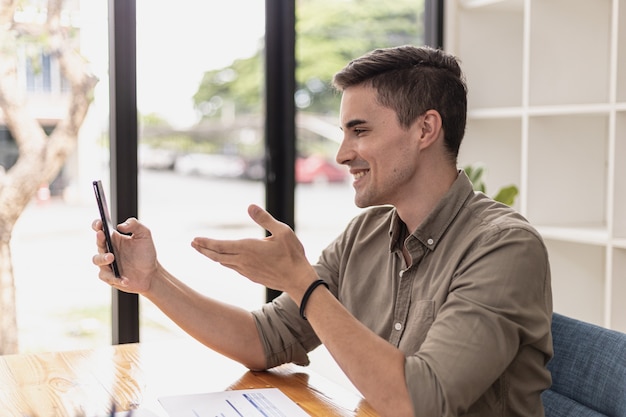 Homem bonito está tendo uma videochamada com uma pessoa em um smartphone. Jovens empresários estão usando smartphones para se comunicarem cara a cara com seus parceiros. Conceito de uso de tecnologia de comunicação.