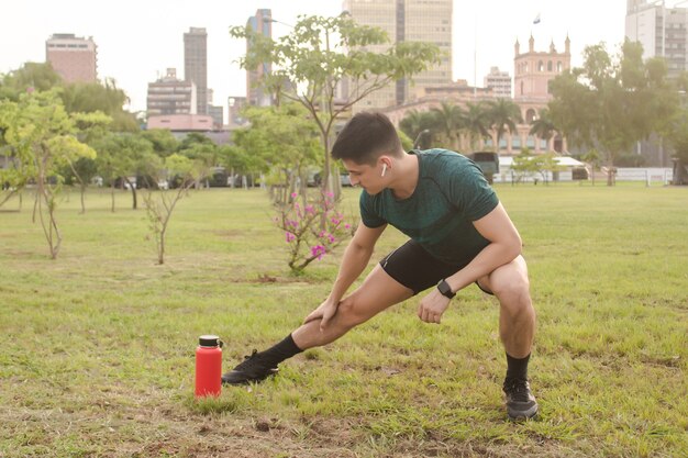 Homem bonito, estendendo-se no parque com a cidade ao fundo.