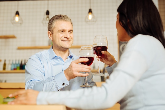 Homem bonito, exuberante e bem constituído e uma mulher de cabelos escuros sentados juntos, bebendo vinho e jantando