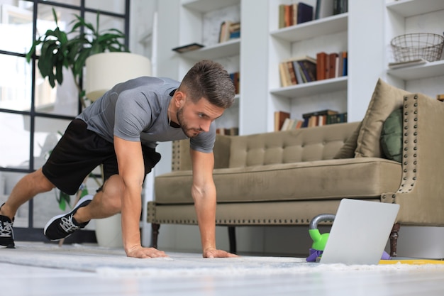 Homem bonito, fazendo exercícios de esporte em casa durante a quarentena. Conceito de vida saudável