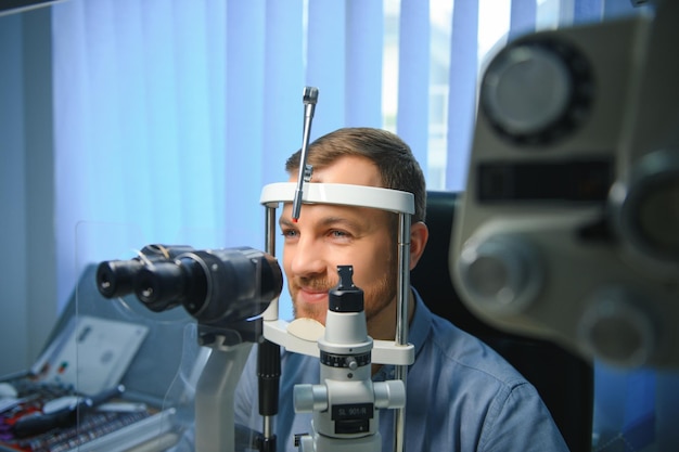 Homem bonito, fazendo um exame oftalmológico na clínica oftalmológica, verificando a retina de um olho masculino fechado