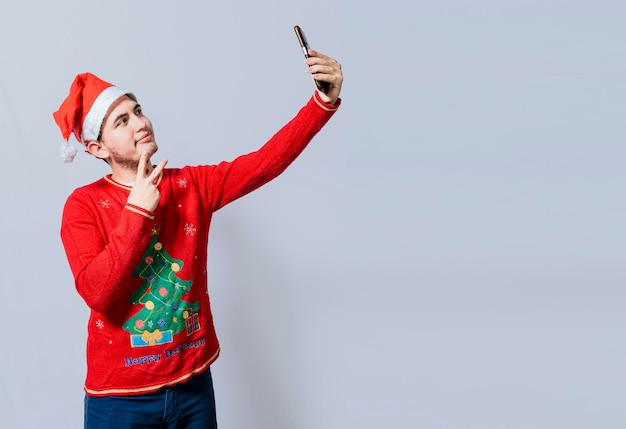 Homem bonito feliz com chapéu de natal tirando uma selfie Cara feliz tirando uma selfie de natal em fundo isolado Jovem sorridente com chapéu de natal tirando uma selfie isolada