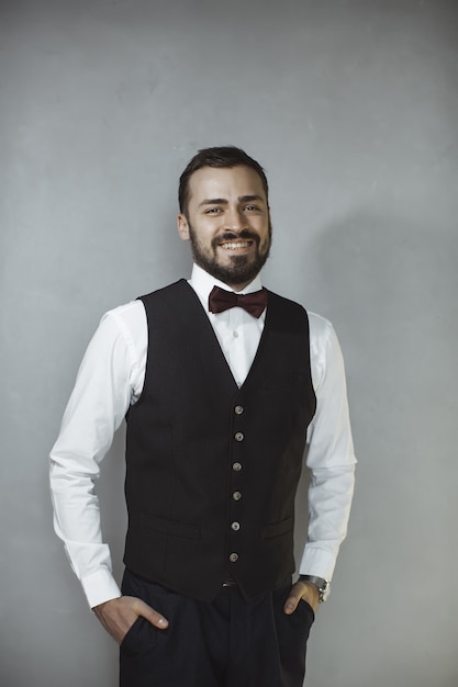 Homem bonito feliz e sorridente de colete preto e gravata borboleta, olhando para a câmera.