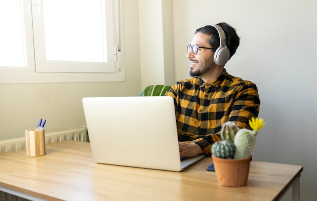 Homem bonito feliz sentado em um escritório enquanto digita em um computador e usa fones de ouvido