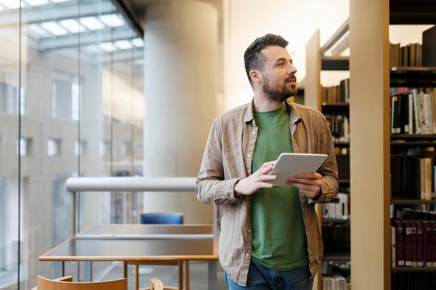 Homem bonito fica na biblioteca da universidade usa tablet digital desvia o olhar estudante latino