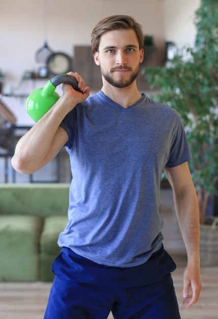 Homem bonito focado em levantar halteres durante um exercício em casa durante a quarentena.