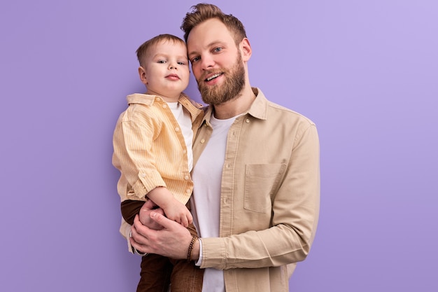 Homem bonito gosta de passar o tempo com o filho, em roupa casual, posando, jogando. Família amigável isolada em fundo roxo