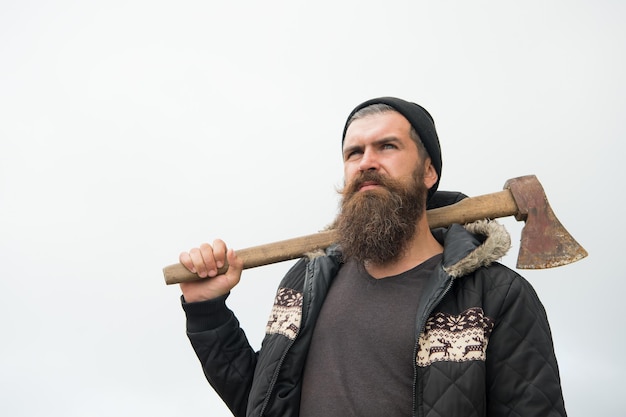 Homem bonito hipster ou cara com barba e bigode na cara séria no chapéu e jaqueta detém machado enferrujado com cabo de madeira ao ar livre no topo da montanha contra céu nublado no fundo natural homem barbudo