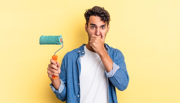 Homem bonito hispânico cobrindo a boca com as mãos com um choque. conceito de pintura a rolo