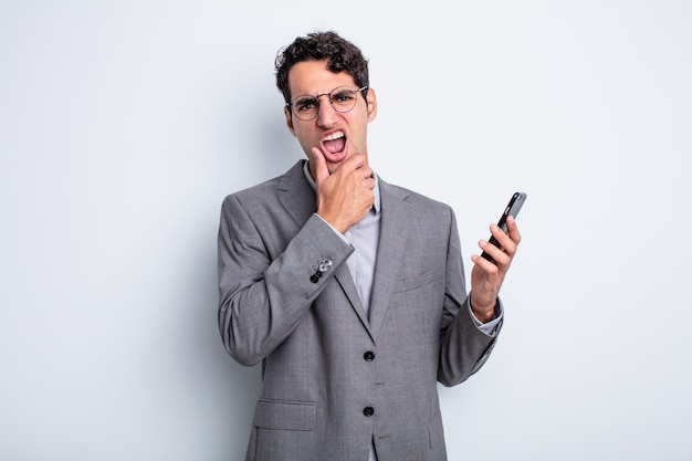 Homem bonito hispânico com boca e olhos bem abertos e mão no queixo. conceito de negócios e telefone