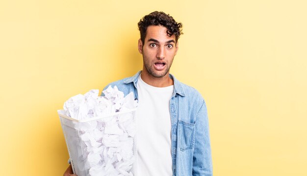 Homem bonito hispânico olhando muito chocado ou surpreso. conceito de lixo de bolas de papel