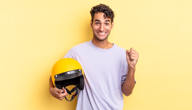 Homem bonito hispânico se sentindo chocado, rindo e comemorando o sucesso. conceito de capacete de motocicleta