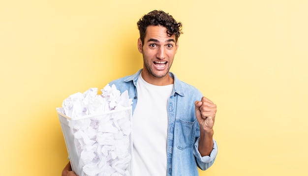 Homem bonito hispânico se sentindo chocado, rindo e comemorando o sucesso. conceito de lixo de bolas de papel