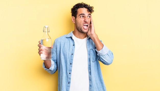 Homem bonito hispânico se sentindo feliz, animado e surpreso. conceito de garrafa de água