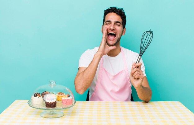 Homem bonito hispânico se sentindo feliz dando um grande grito com as mãos ao lado da boca bolos caseiros cocnept