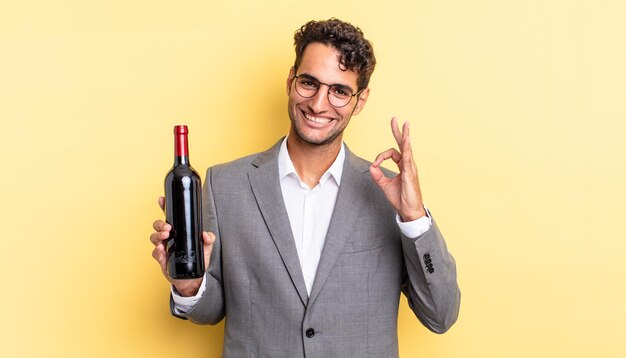 Homem bonito hispânico se sentindo feliz, mostrando aprovação com um gesto certo. conceito de garrafa de vinho