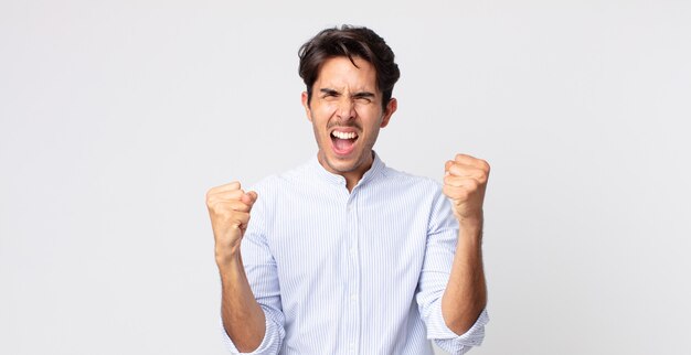 Homem bonito hispânico se sentindo feliz, positivo e bem-sucedido, comemorando a vitória, conquistas ou boa sorte