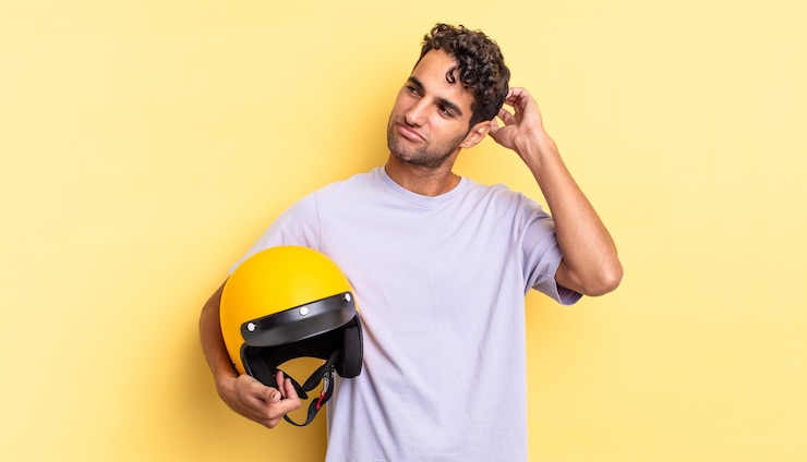 Foto homem bonito hispânico se sentindo perplexo e confuso, coçando a cabeça. conceito de capacete de motocicleta