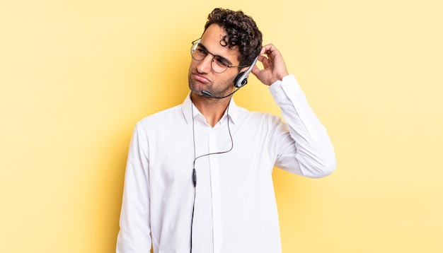 Homem bonito hispânico se sentindo perplexo e confuso, coçando a cabeça. conceito de telemarketing