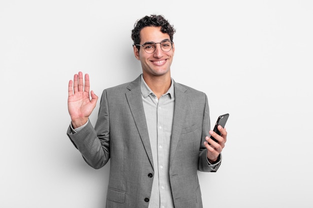 Homem bonito hispânico sorrindo alegremente, acenando com a mão, dando as boas-vindas e cumprimentando você. conceito de negócios e telefone