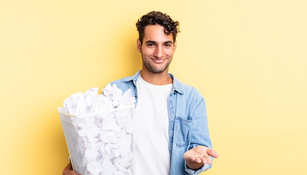 Homem bonito hispânico, sorrindo alegremente com simpáticos e oferecendo e mostrando um conceito. conceito de lixo de bolas de papel