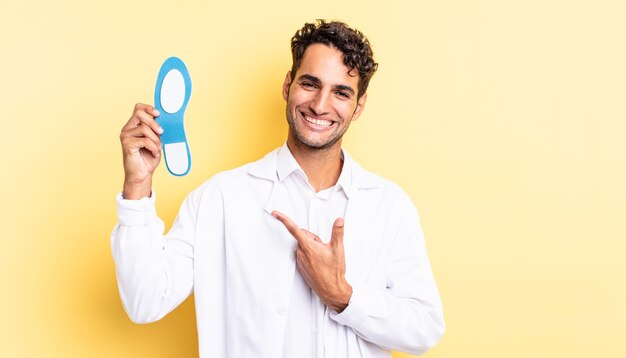 Homem bonito hispânico sorrindo alegremente, sentindo-se feliz e apontando para o lado. conceito de quiropodista