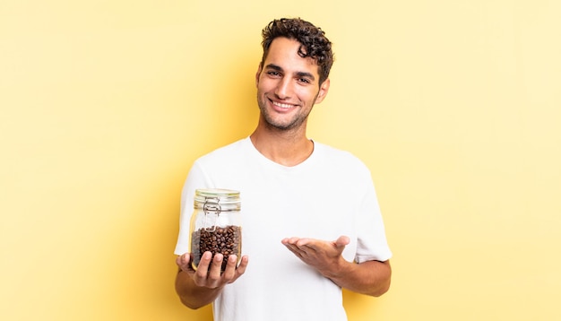 Homem bonito hispânico sorrindo alegremente, sentindo-se feliz e mostrando um conceito. garrafa de grãos de café