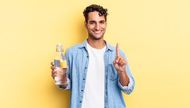 Homem bonito hispânico sorrindo com orgulho e confiança, fazendo o conceito de garrafa de água número um