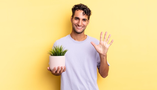 Homem bonito hispânico sorrindo e parecendo amigável mostrando o conceito de planta decorativa número cinco