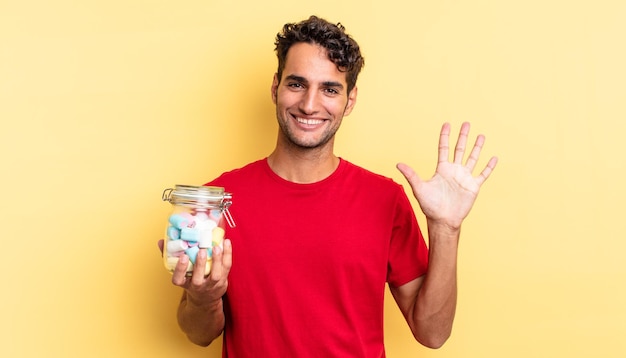 Homem bonito hispânico sorrindo e parecendo amigável, mostrando o número cinco. conceito de doces