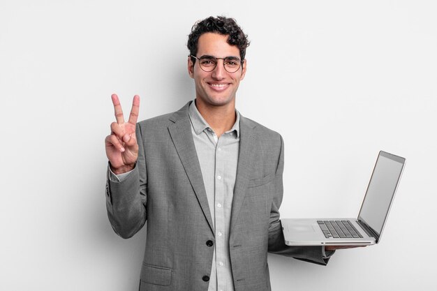 Homem bonito hispânico sorrindo e parecendo amigável, mostrando o número dois. conceito de negócios e laptop