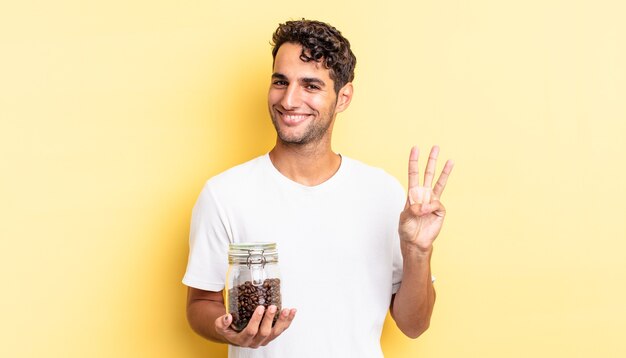 Homem bonito hispânico sorrindo e parecendo amigável, mostrando o número três. garrafa de grãos de café