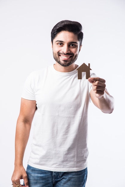 Homem bonito indiano segurando um modelo de casa em 3D feito de papel - conceito imobiliário