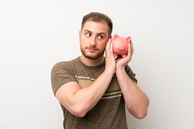 Homem bonito isolado parede branca segurando um grande piggybank