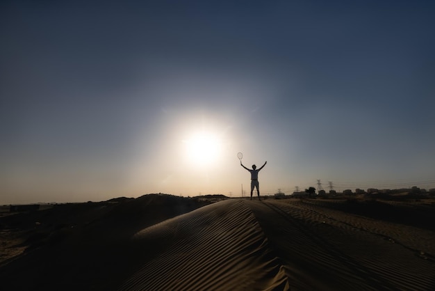 Homem bonito jogando tênis em um barkhan no deserto. Pôr do sol. Esporte. tribunais