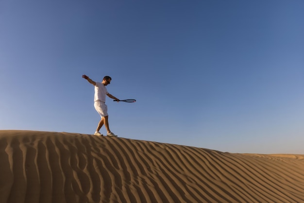 Homem bonito jogando tênis em um barkhan no deserto. Pôr do sol. Esporte. tribunais