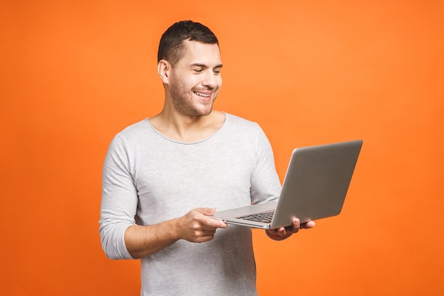 Homem bonito jovem confiante casual segurando laptop e sorrindo em pé contra um fundo laranja