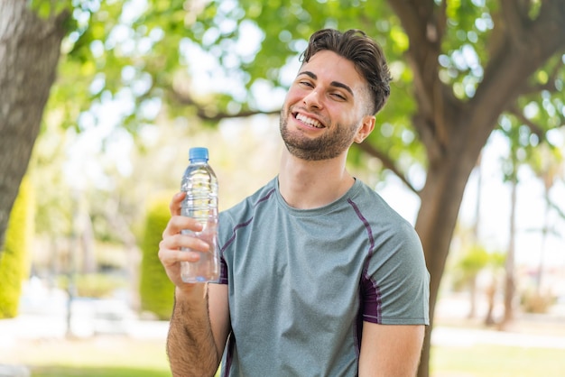 Foto homem bonito jovem esporte com uma garrafa de água ao ar livre sorrindo muito