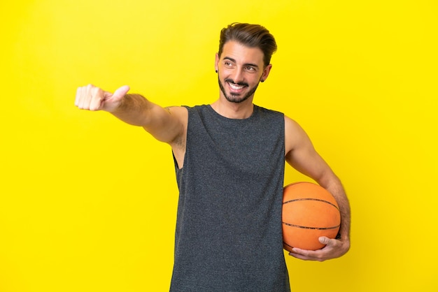 Homem bonito jovem jogador de basquete isolado em fundo amarelo dando um polegar para cima gesto