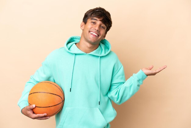 Homem bonito jovem jogador de basquete isolado em fundo ocre, estendendo as mãos para o lado para convidar para vir