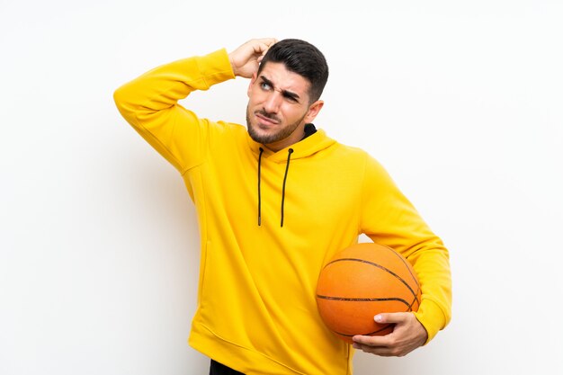 Homem bonito jovem jogador de basquete sobre parede branca isolada, tendo dúvidas e com a expressão do rosto confuso