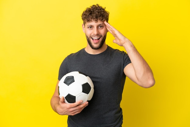 Homem bonito jovem jogador de futebol isolado em fundo amarelo com expressão de surpresa