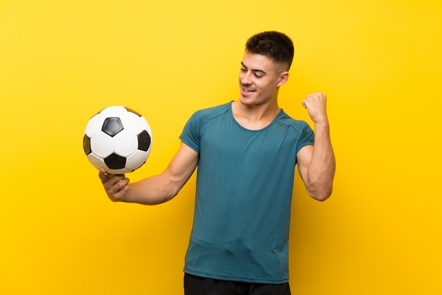 Homem bonito jovem jogador de futebol isolado parede amarela comemorando uma vitória