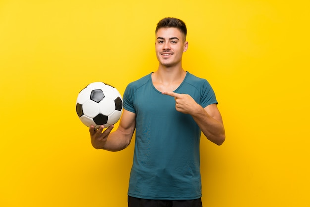 Homem bonito jovem jogador de futebol isolado parede amarela e apontando-o