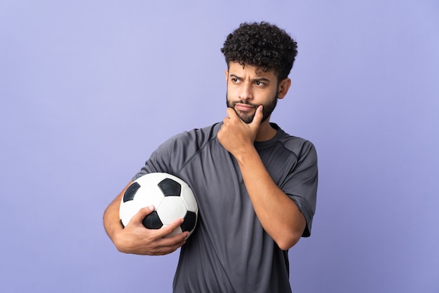 Homem bonito jovem jogador de futebol marroquino isolado na parede roxa, tendo dúvidas