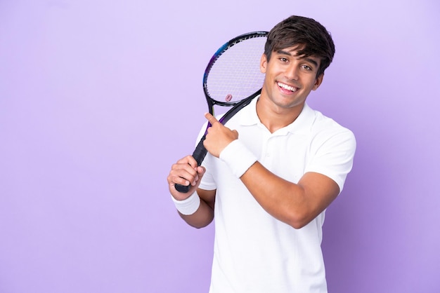 Homem bonito jovem jogador de tênis isolado em fundo ocre, apontando para trás