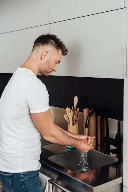 Homem bonito lavando as mãos perto da pia na cozinha