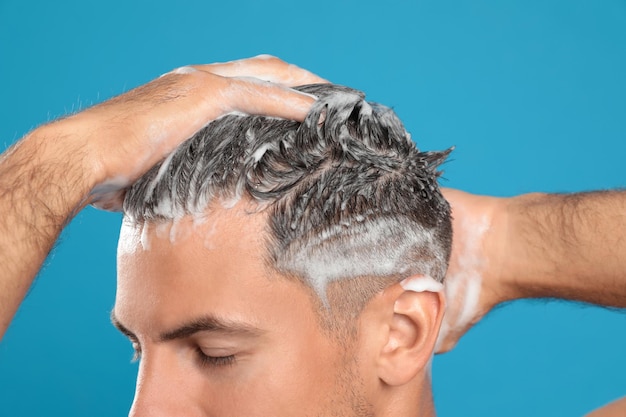 Homem bonito, lavando o cabelo em closeup de fundo azul claro