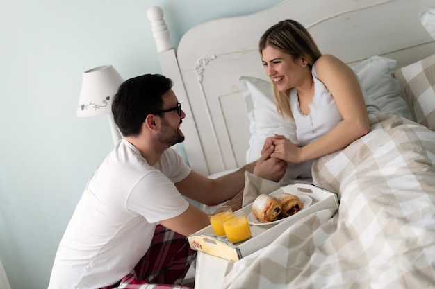 Homem bonito levando café da manhã para sua linda namorada na cama